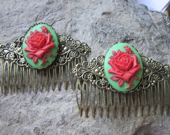 May include: Two gold hair combs with a green and red rose design. Each comb has a large oval cameo with a red rose on a green background. The combs are ornate and have a delicate filigree design.