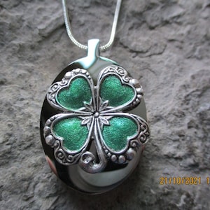 May include: Silver oval locket necklace with a green four-leaf clover charm. The clover has a silver filigree design and a sparkly green enamel finish.