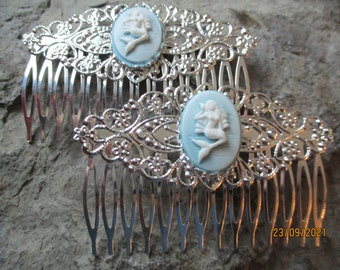 May include: Two silver hair combs with a blue and white cameo of a mermaid. The combs have a decorative floral design.