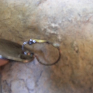 Puede incluir: Un pendiente de plata con una peque&ntilde;a piedra redonda y transparente. El pendiente es de estilo aro con cierre de bisagra.