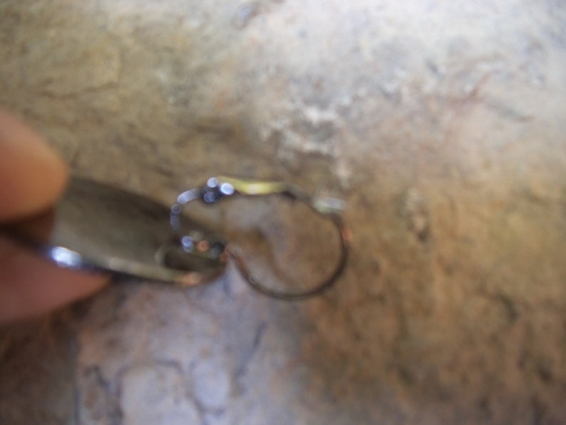 Puede incluir: Un pendiente de plata con una peque&ntilde;a piedra redonda y transparente. El pendiente es de estilo aro con cierre de bisagra.