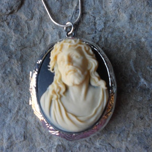 Può includere: Una collana con un ciondolo a forma di medaglione in argento con un cammeo di Gesù Cristo. Il cammeo è bianco e lo sfondo è nero.