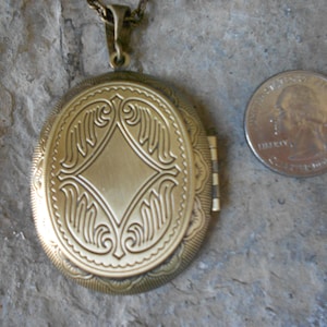 Pode incluir: Um medalh&atilde;o oval de metal dourado com um design intrincado na frente. O medalh&atilde;o &eacute; aproximadamente do tamanho de uma moeda de 25 centavos.