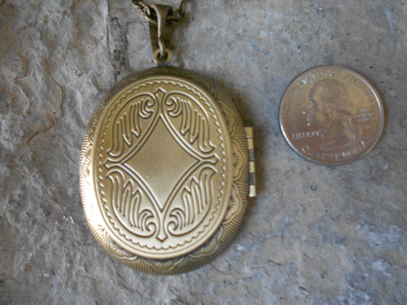 Pode incluir: Um medalh&atilde;o oval de metal dourado com um design intrincado na frente. O medalh&atilde;o &eacute; aproximadamente do tamanho de uma moeda de 25 centavos.