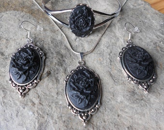 May include: A black cameo jewelry set with a necklace, bracelet, and earrings. Each piece features a black rose design in an oval silver frame.