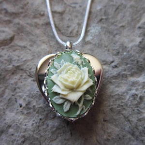 May include: A silver heart-shaped locket necklace with a cameo of a white rose on a green background.