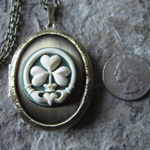 May include: A gold-tone oval locket necklace with a green and white cameo of a shamrock and a Claddagh ring. The locket is about the size of a quarter.