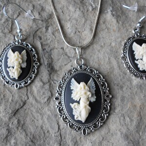May include: A silver necklace and earrings set with black cameo pendants featuring white angel figures.