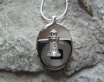 May include: A silver oval locket necklace with a silver lighthouse charm. The locket has a smooth, shiny surface.