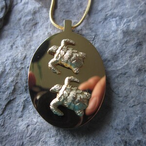 May include: Gold pendant necklace featuring two detailed turtle designs on a round, polished surface.