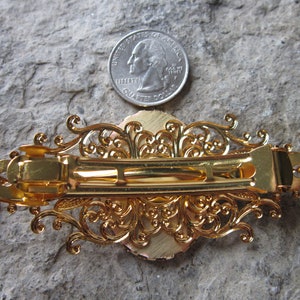 May include: Gold-toned hair clip with an ornate filigree design. The clip is about the size of a US quarter.
