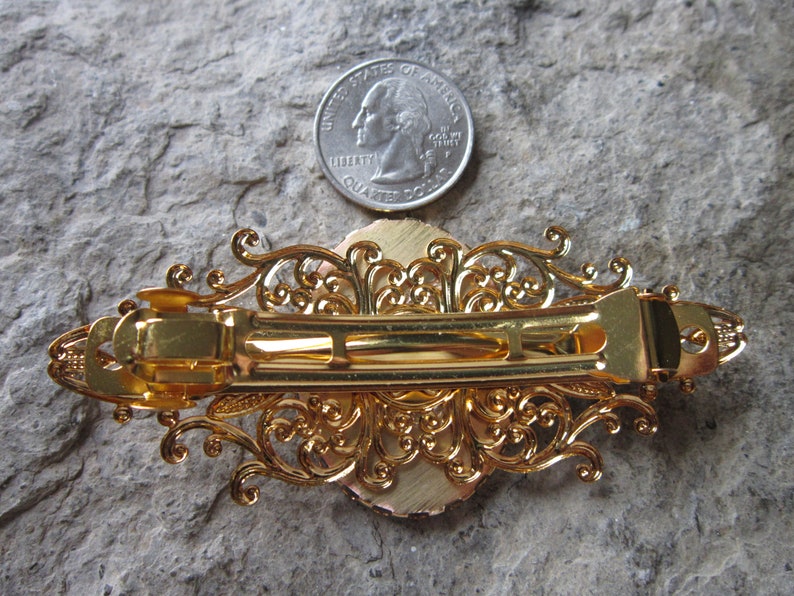May include: Gold-toned hair clip with an ornate filigree design. The clip is about the size of a US quarter.