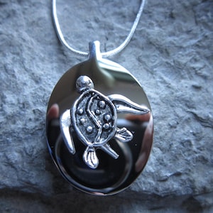 May include: A silver pendant necklace featuring a detailed turtle design with a yin yang symbol on its shell. The pendant is oval shaped and hangs from a silver chain.