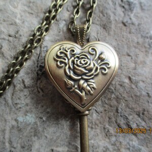 K&ouml;nnte beinhalten: Eine Halskette mit Anh&auml;nger im Vintage-Stil aus Messing. Der herzf&ouml;rmige Medaillonanh&auml;nger zeigt ein Rosenmuster und h&auml;ngt an einer passenden Kette. Das Medaillon ist mit einem gepr&auml;gten Rosen- und Bl&auml;ttermuster versehen.