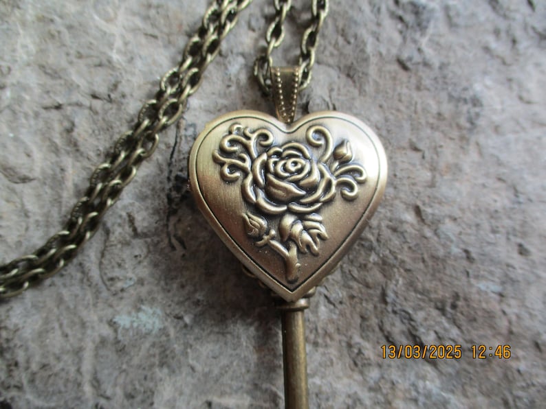 K&ouml;nnte beinhalten: Eine Halskette mit Anh&auml;nger im Vintage-Stil aus Messing. Der herzf&ouml;rmige Medaillonanh&auml;nger zeigt ein Rosenmuster und h&auml;ngt an einer passenden Kette. Das Medaillon ist mit einem gepr&auml;gten Rosen- und Bl&auml;ttermuster versehen.