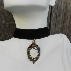 May include: A black velvet choker necklace with a cameo pendant featuring a white rose in a gold frame.