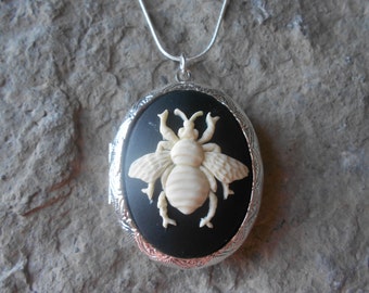 May include: A silver locket necklace with a black cameo featuring a white bee design.