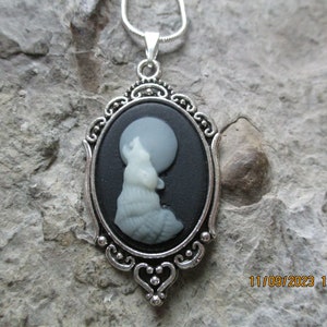May include: A silver pendant necklace with a black cameo featuring a white wolf howling at the moon.