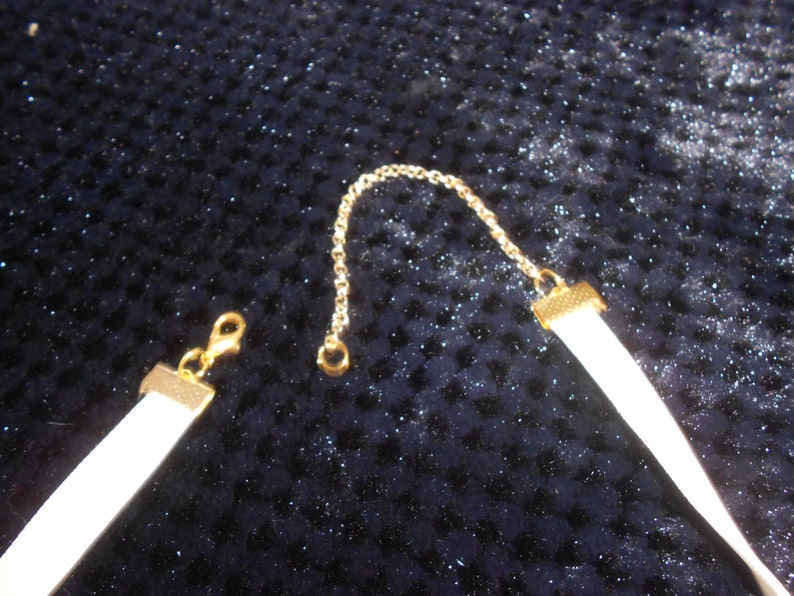 May include: A white choker necklace with a gold chain and clasp. The necklace is made of a soft, pliable material.