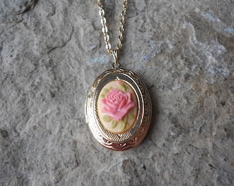 Puede incluir: Collar con dije de oro con un camafeo de rosa rosa. El dije es de forma ovalada y tiene un diseño detallado alrededor del borde.
