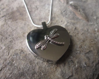 May include: A silver heart-shaped pendant necklace with a dragonfly design. The pendant has a small opening on the side.