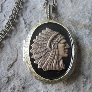 May include: A bronze locket necklace with a detailed image of a Native American chief wearing a headdress. The locket has a black background and a decorative border.