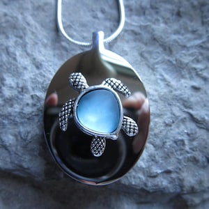 May include: A silver pendant necklace with a blue glass turtle charm. The turtle is on a round silver disc.