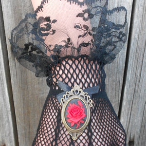 May include: Black lace and fishnet gloves with a vintage-style brooch featuring a red rose.