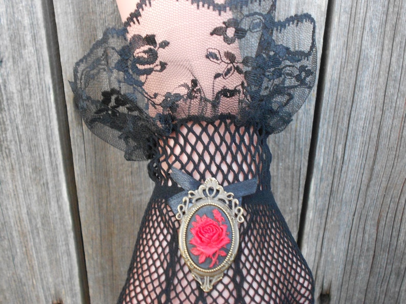 May include: Black lace and fishnet gloves with a vintage-style brooch featuring a red rose.