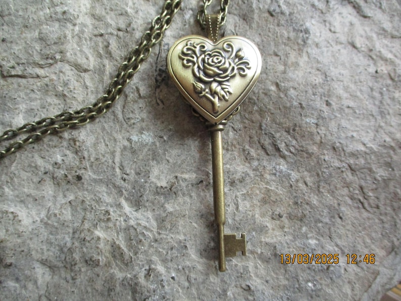 K&ouml;nnte beinhalten: Halskette im Vintage-Stil mit einem bronzefarbenen Schl&uuml;sselanh&auml;nger. Der Anh&auml;nger hat ein herzf&ouml;rmiges Medaillon mit einem Rosendesign. Der Schl&uuml;ssel h&auml;ngt an einer passenden Kette und erzeugt eine romantische und antike &Auml;sthetik.