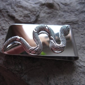 Puede incluir: Un clip de dinero de plata con un diseño de serpiente detallado. La serpiente está enroscada con la cabeza levantada.