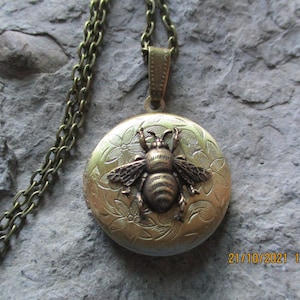 May include: A gold locket necklace with a bee design. The locket is engraved with floral patterns and has a detailed bee charm.