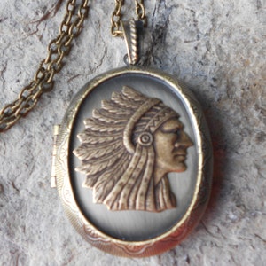 May include: A bronze oval locket necklace with a detailed image of a Native American chief wearing a headdress. The locket has a hinged opening.
