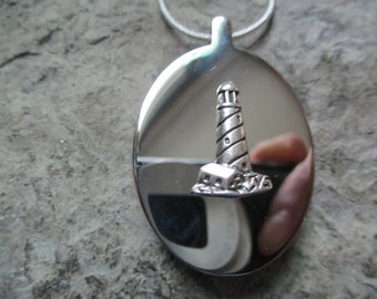 May include: Silver oval pendant necklace with a silver lighthouse charm. The pendant is on a silver chain.
