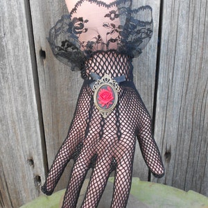 May include: Black fishnet gloves with a black lace cuff and a gold-toned brooch featuring a red rose.