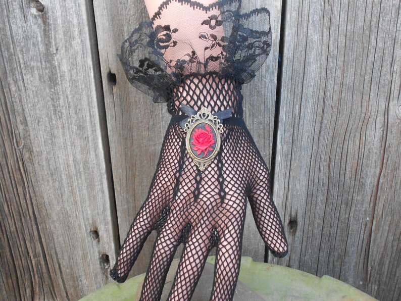 May include: Black fishnet gloves with a black lace cuff and a gold-toned brooch featuring a red rose.