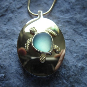 May include: A gold oval locket necklace with a green sea turtle charm. The turtle has a light blue glass centre.