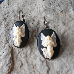 Puede incluir: Un par de pendientes de camafeo negro con un dise&ntilde;o de &aacute;ngel blanco. Los pendientes tienen un cierre de gancho plateado.