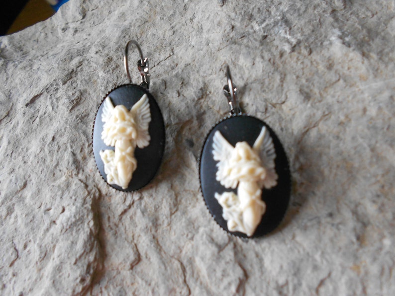 Puede incluir: Un par de pendientes de camafeo negro con un dise&ntilde;o de &aacute;ngel blanco. Los pendientes tienen un cierre de gancho plateado.