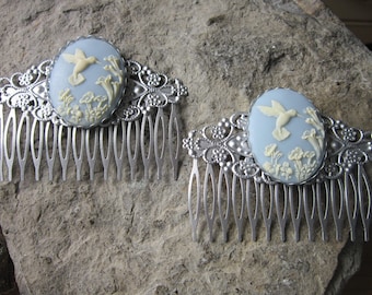 May include: Two silver hair combs with blue and white cameo-style embellishments featuring a hummingbird in flight. The cameos are surrounded by ornate silver filigree.