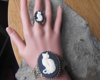 May include: A black and white cameo ring and bracelet featuring a white cat design. The ring is on the index finger of a hand, and the bracelet is on the wrist.