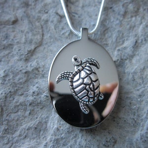 May include: A silver pendant necklace featuring a detailed turtle design. The pendant is round and has a shiny, reflective surface.