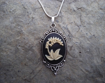 May include: A silver chain necklace with a black cameo pendant featuring a white lily of the valley flower design.