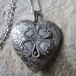 Peut inclure: Collier avec pendentif en forme de cœur argenté orné d'un trèfle à quatre feuilles. Le pendentif a un motif floral complexe et une ouverture à charnière.