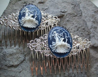 May include: Two silver hair combs with blue and white cameo designs. Each comb features a white cameo of a woman with a deer in a woodland setting. The cameos are set against a dark blue background.
