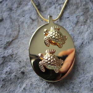 May include: Gold necklace with a round pendant featuring two embossed turtle designs.
