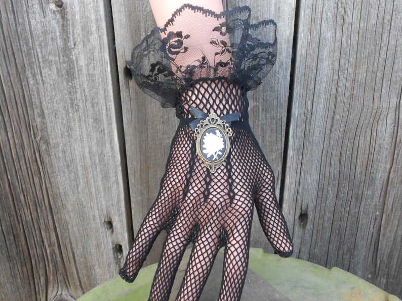 May include: Black fishnet gloves with a lace cuff and a decorative brooch featuring a white cameo.