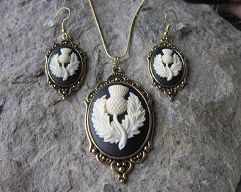 May include: A gold necklace and earrings set with a black and white cameo featuring a thistle flower.