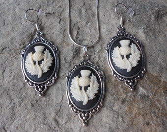 May include: A silver necklace and earrings set with a black cameo featuring a white thistle design.