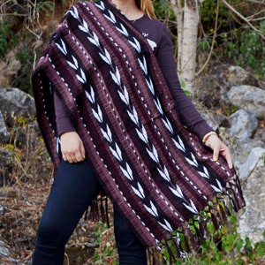 May include: A woman wearing a brown and white striped poncho with fringe. The poncho has a geometric pattern of white arrows on a brown background.
